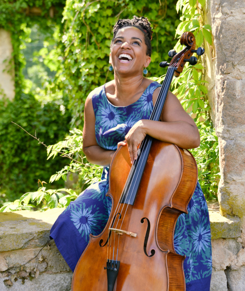 Woman laughs while holding cello outside in sunshine
