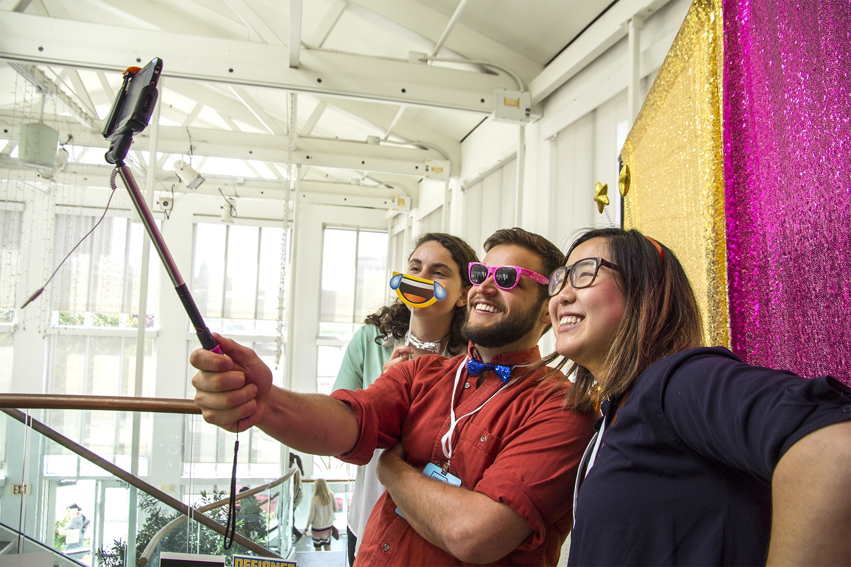 Picture of 3 people taking a selfie using fun props in front of a sparkly backdrop