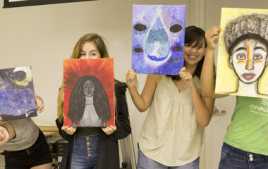 Four teenagers show the camera their paintings and smile