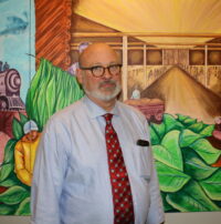 Picture waist up of a man in a button up and tie in front of a painting