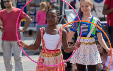 Two girls in bright costumes perform outdoors using hula hoops