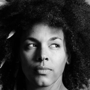 Black and white headshot of woman with feathers poking out of her natural hair