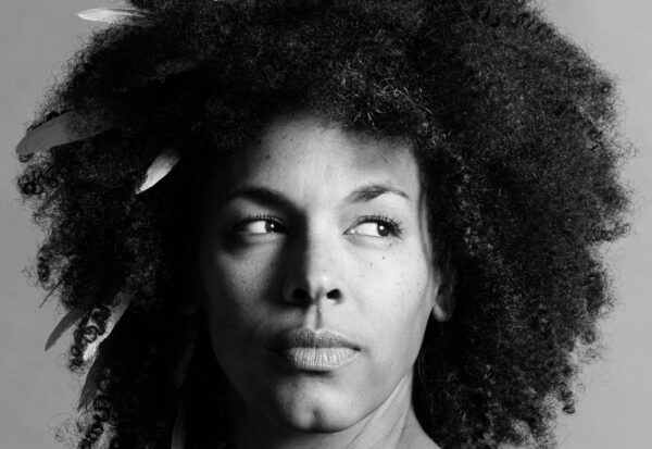 Black and white headshot of woman with feathers poking out of her natural hair