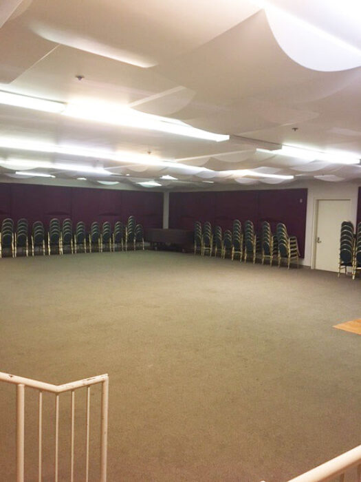Corner view of a basement room with chairs stacked against the walls