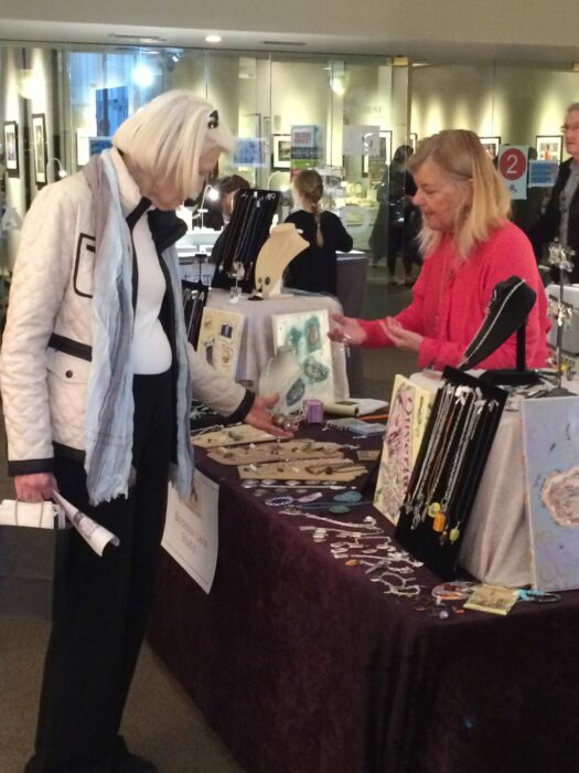 A shopper talks to an artist who is displaying her jewelry at a fair