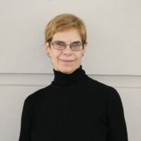 Headshot of woman in black turtleneck in front of a cream wall
