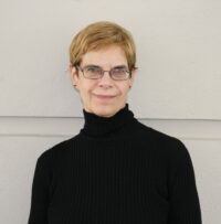 Headshot of woman in black turtleneck in front of a cream wall
