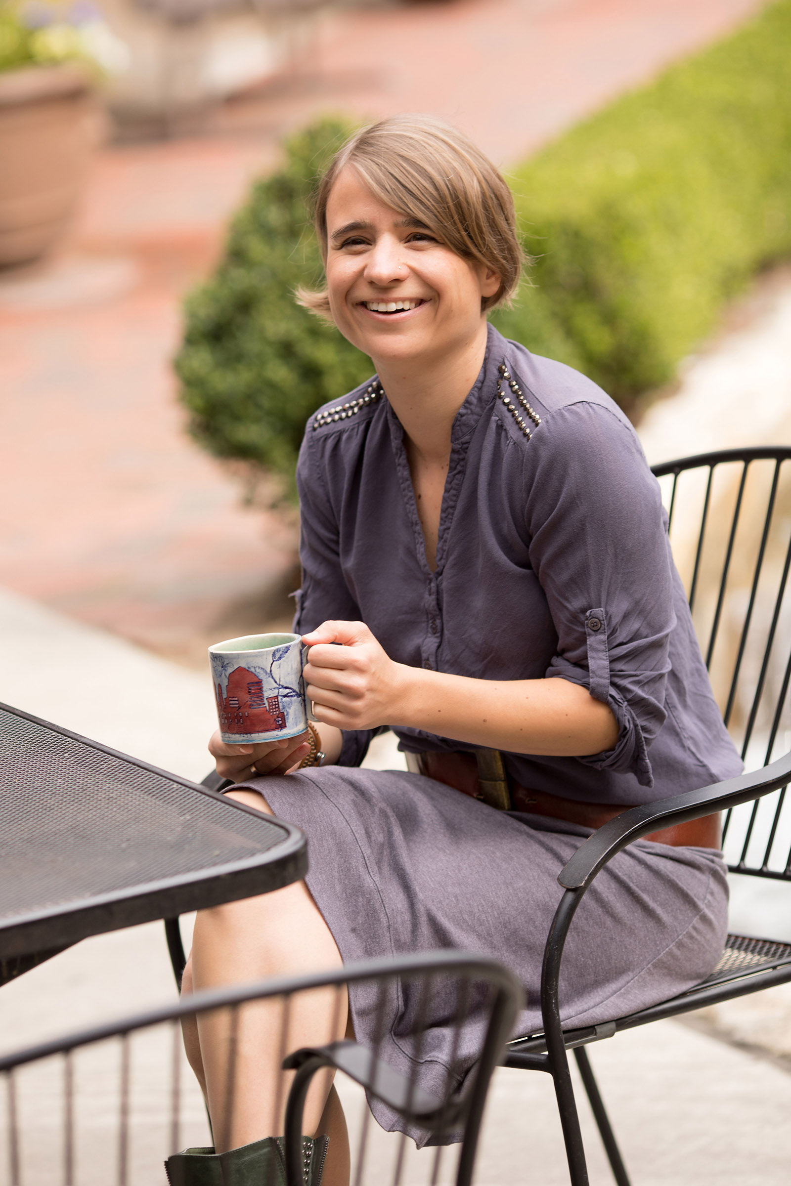 A woman sits at a patio table holding a mug and laughing