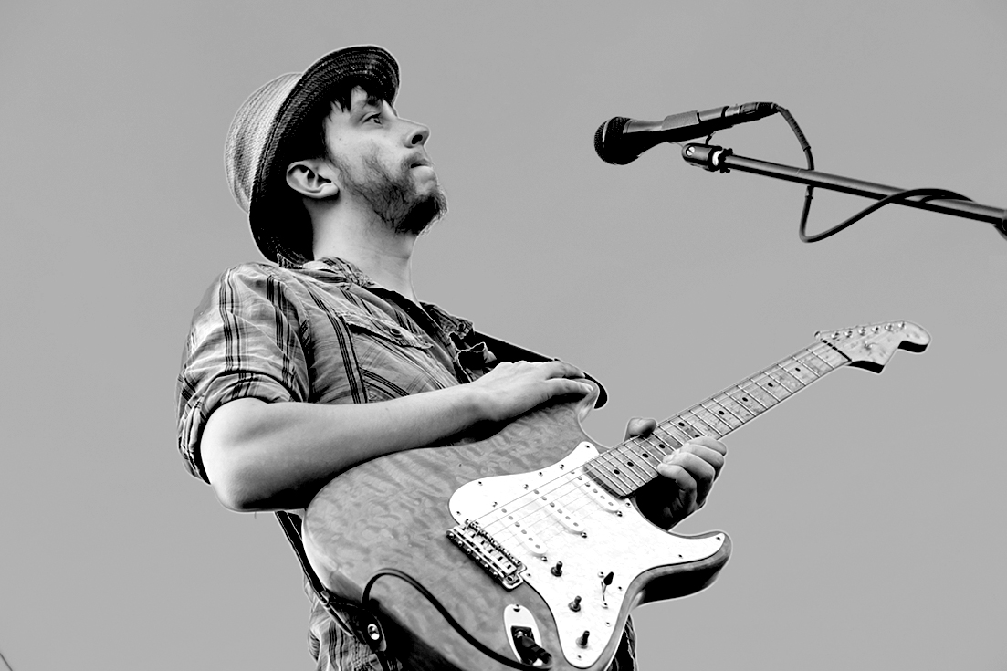 Black and white image of a man holding a guitar standing behind a microphone