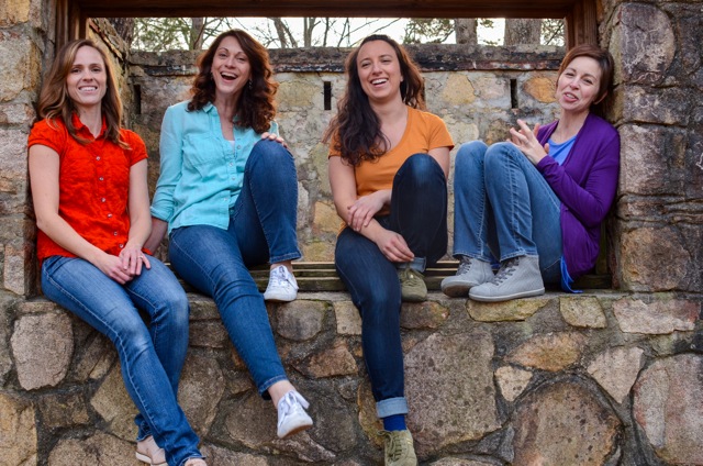 Four women sit together in a stone alcove laughing