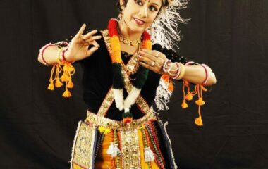 A dancer poses dressed in elaborate, bright traditional Indian costuming