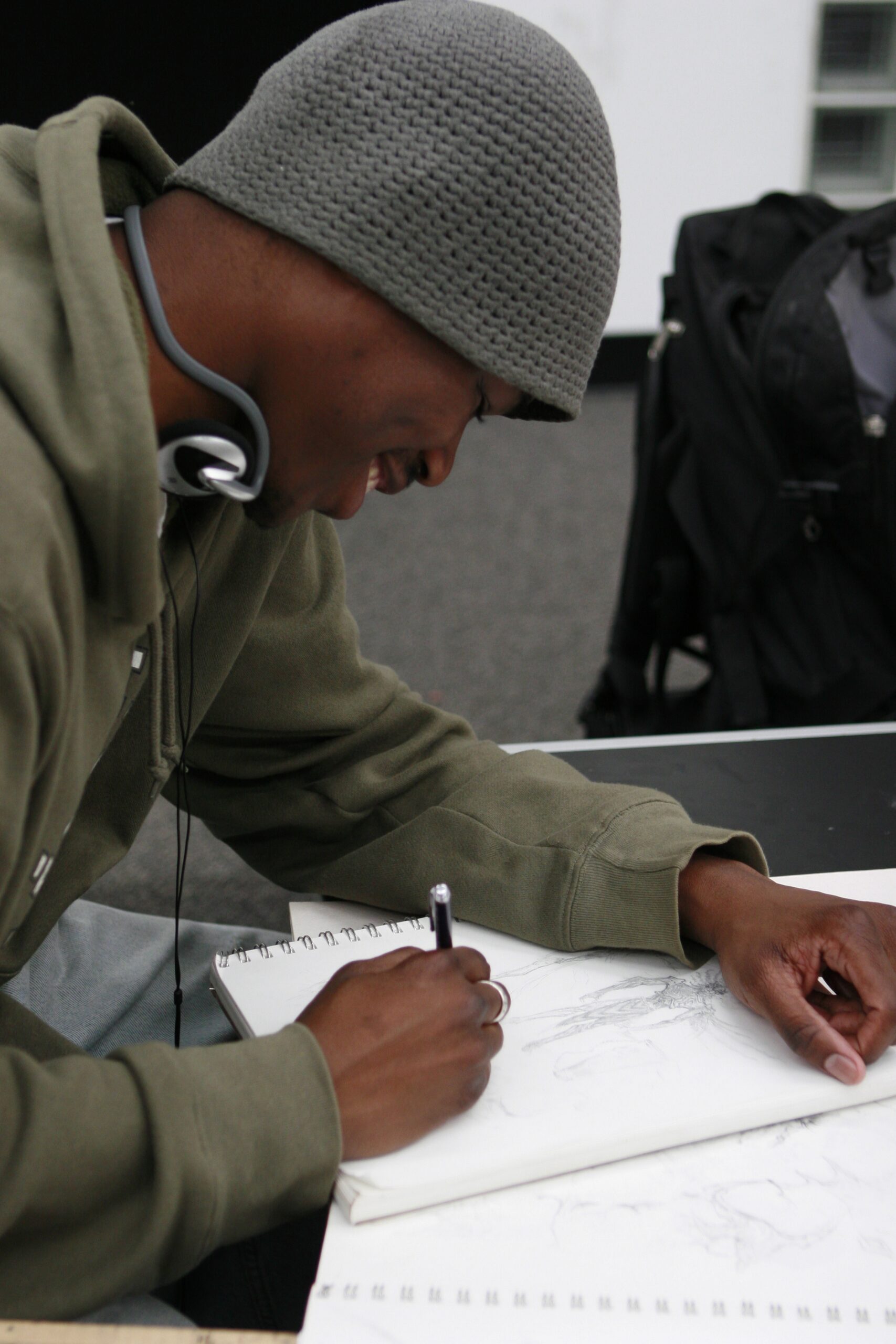 An artist draws in their sketchbook wearing a beanie