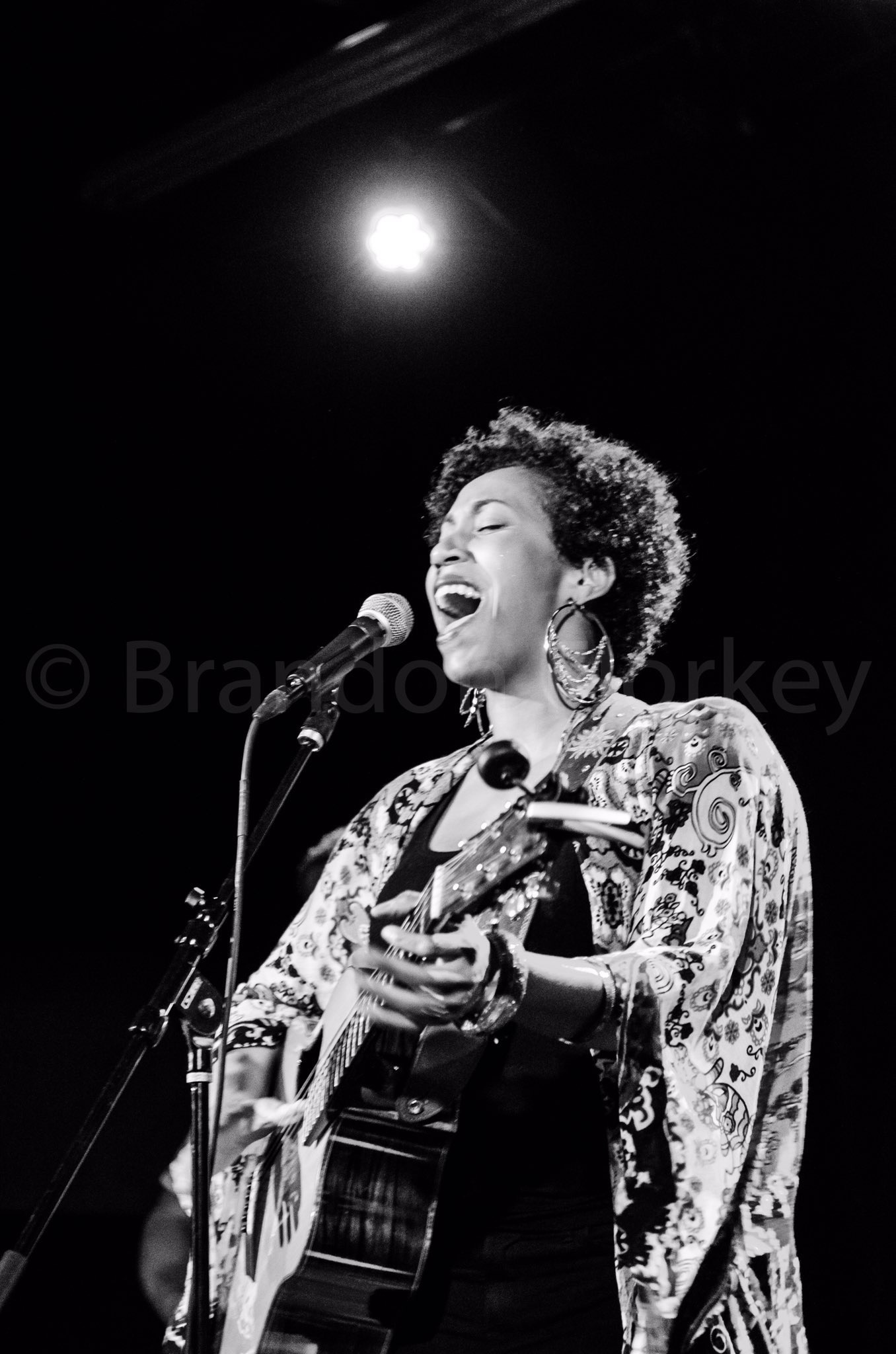 Black and white image of a woman playing acoustic guitar and singing into a microphone