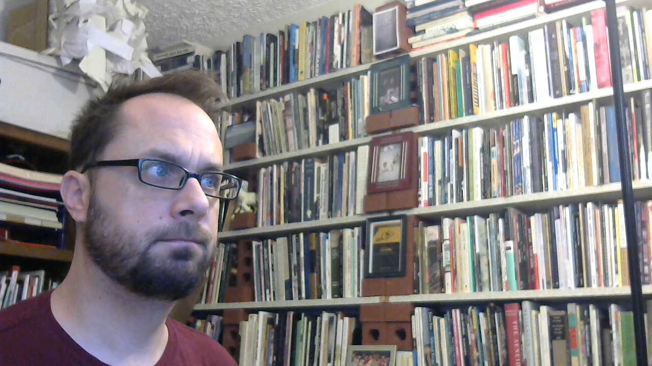 Closeup of a man sitting in front of a very full bookcase
