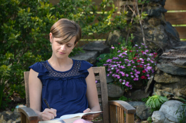 A woman sits on a garden chair writing in a book