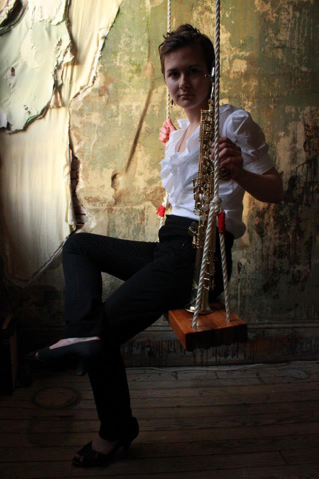 A musician sits on a swing with legs crossed and holds a woodwind instrument