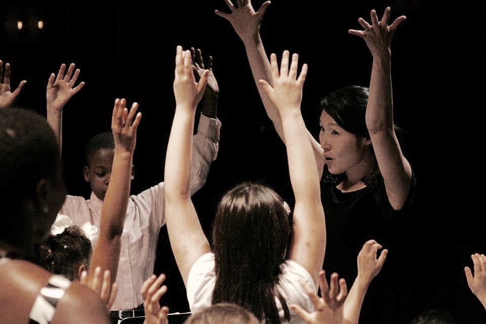 A woman and a group of children have their hands raised in the air
